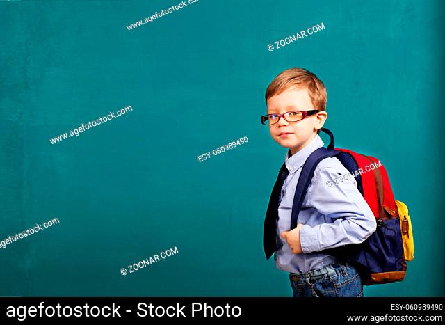 School, kid, rucksack. little Boy in eyeglasses. Cheerful smiling little kid with big backpack against chalkboard. Looking at camera. School concept