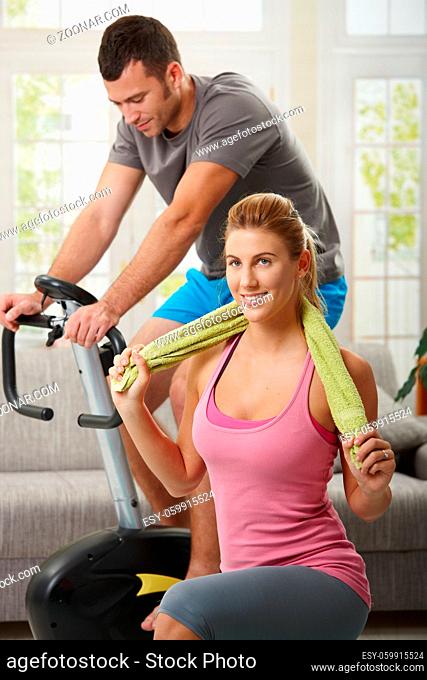 Man training on exercise bike, woman doing streching exercise on fitness mat at home