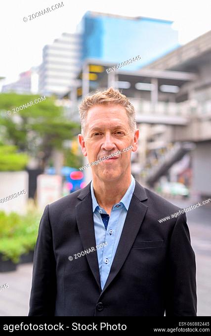 Portrait of mature businessman in suit against view of the sky train station in the city