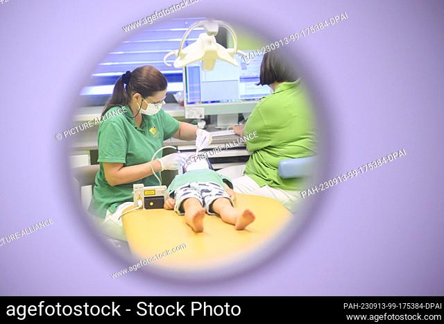 PRODUCTION - 11 September 2023, Lower Saxony, Hanover: A pediatric dentist (l) examines a three-year-old child in a pediatric dental practice - photographed...