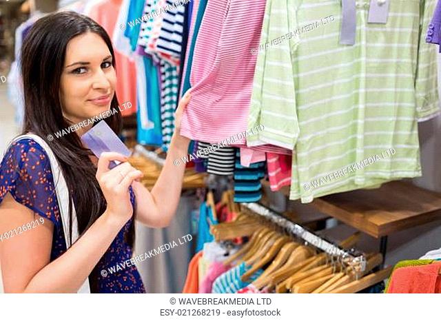 Woman holding credit card beside clothing display in clothes store
