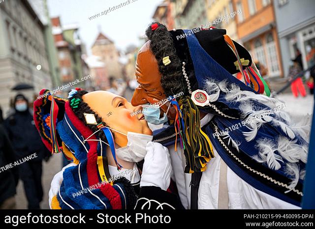 dpatop - 15 February 2021, Rottweil: Two jesters wearing masks over their Carnival masks kiss during a parade in the town of Rottweil.