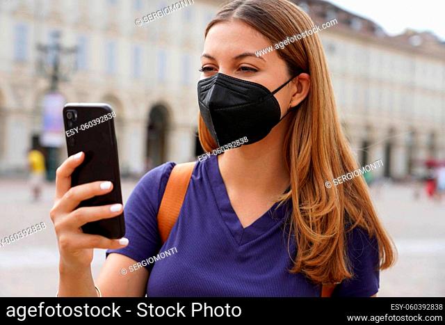 Close up of girl with black protective mask FFP2 KN95 using smart phone with urban background