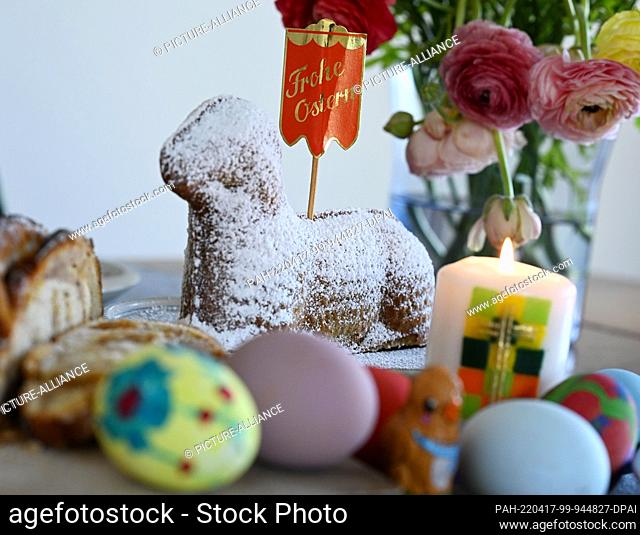 17 April 2022, Bavaria, Garmisch-Partenkirchen: Traditional Easter foods such as an Easter plait, colorful Easter eggs and an Easter lamb are set on a table...