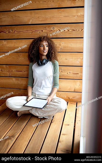 Young woman with digital tablet looking away while sitting with cross-legged at home