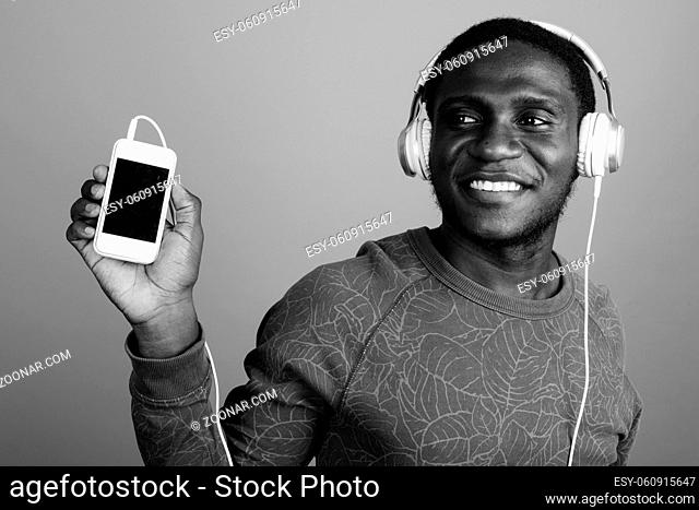 Studio shot of young African man wearing long sleeved shirt against gray background in black and white