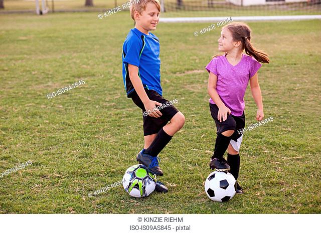 Boy and younger sister with footballs on practice pitch