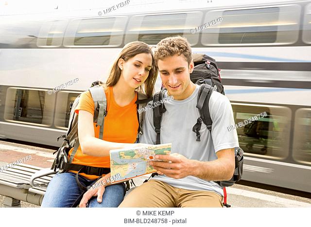Caucasian couples sitting on bench near train reading map
