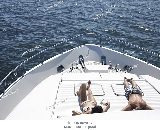 Young couple sunbathing on bow of yacht at sea elevated view