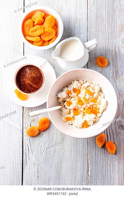 Breakfast from cottage cheese with slices of dried apricot and cup of black coffee on white wooden background. Top view