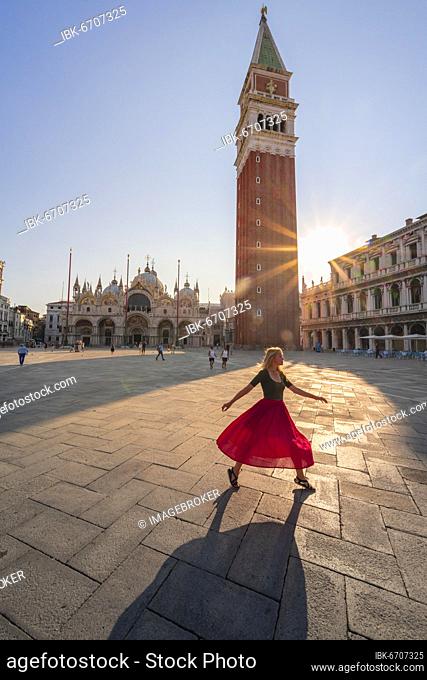 Young woman, tourist with red dress at St. Mark's Square, sun shines on St. Mark's Square with Campanile di San Marco, Venice, Veneto, Italy, Europe