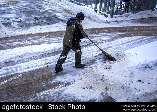05 December 2023, Mecklenburg-Western Pomerania, Wismar: A footpath at the pier is cleared of snow with a snow shovel. Heavy snowfall and temperatures below...