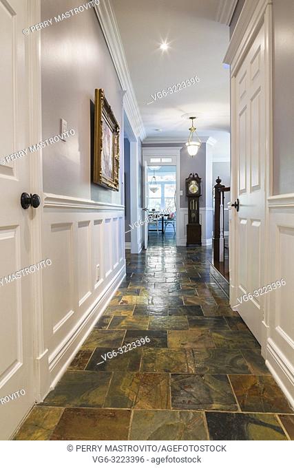 Ground floor hallway with earth tone slate flooring leading to the kitchen inside a contemporary cottage style home