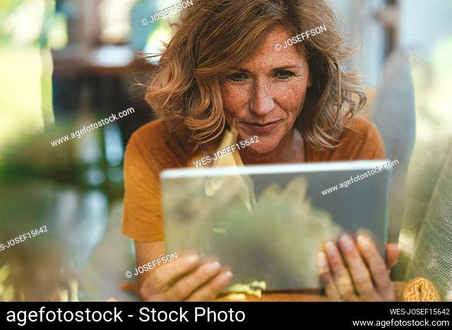 Mature woman using tablet PC seen through glass window