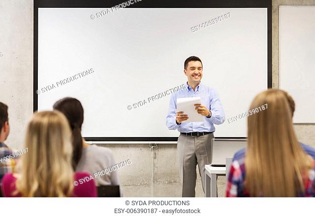 education, high school, technology and people concept - smiling teacher with notepad, laptop computer standing in front of students and showing something on...