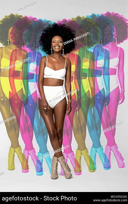 Smiling Afro woman with multiple exposure standing against white background
