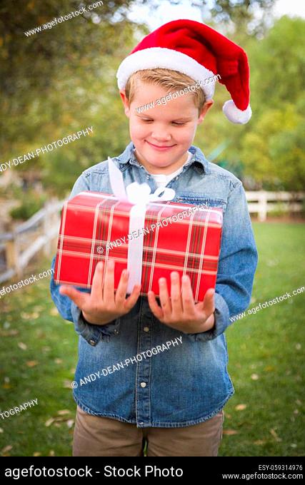 Handsome Young Boy Wearing Santa Hat Holding Christmas Gift Outside