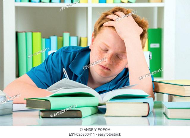 Exhausted Boy Studying In Library With Books On Desk