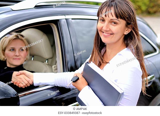 Happy attractive saleslady finalising a deal shaking hands with a blond woman who has just purchased a new car from her