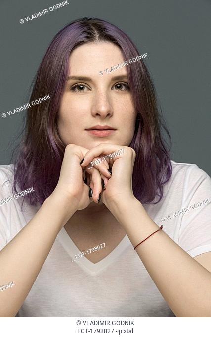 Portrait of a young woman with dyed hair and resting chin on hands against gray background