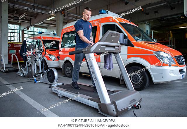 10 January 2019, North Rhine-Westphalia, Gelsenkirchen: The fireman Tom runs on a treadmill in the fire station in front of parked rescue vehicles