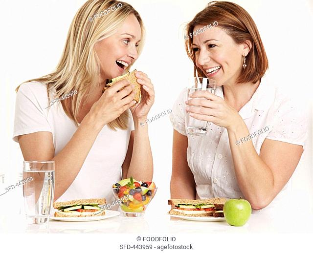 Two women eating sandwiches and drinking water