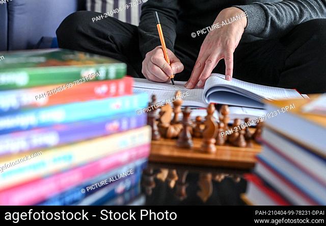 01 April 2021, Berlin: Surrounded by chess books in his apartment, the chess player Heiermann writes his next move on a postcard in correspondence chess