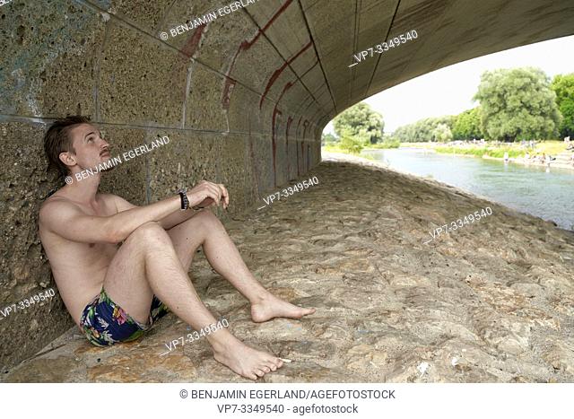 man sitting under bridge Wittelsbacherbrücke at river Isar, in Munich, Germany