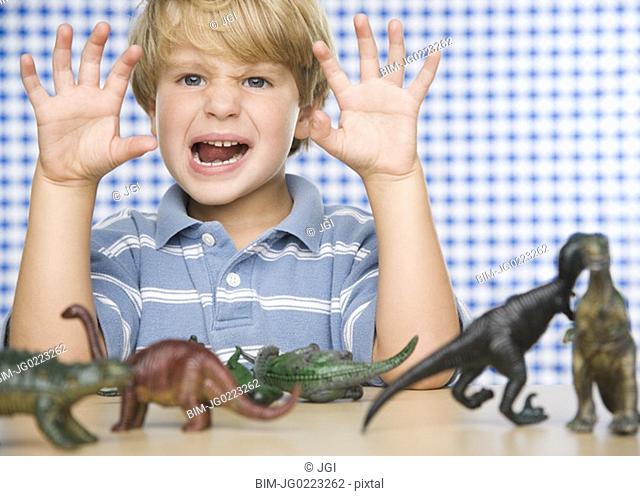 Young boy making face with toy dinosaurs