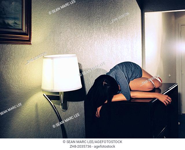 A young woman lies seductively and mysteriously on a cabinet in a room