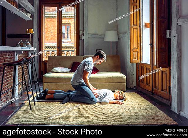 Young man massaging girlfriend lying on rug in living room at home