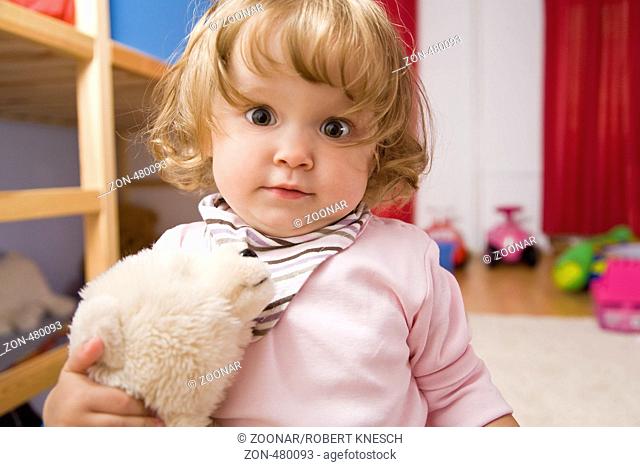 Einjähriges Mädchen steht mit Stofftier unter dem Arm im Kinderzimmer