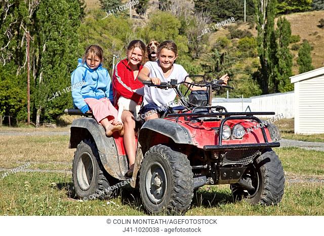 Upcot Station girls with pet spaniel ride quad bike on farm, Upper Awatere valley, Marlborough, New Zealand