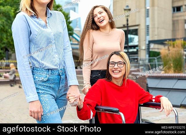 Happy disabled woman on wheelchair spending leisure time with female friends in city