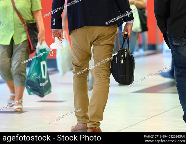 16 July 2021, Saxony, Dresden: A man holds his FFP2 mask in the Elbepark shopping centre. In Saxony, the mask obligation will be relaxed as of today