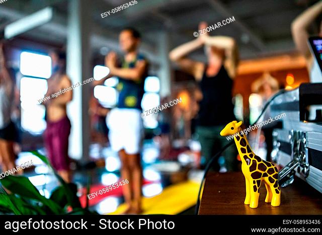 Blurry people are seen standing in pose behind a small table with decorative giraffe figure inside a gym during 108 sun salutations