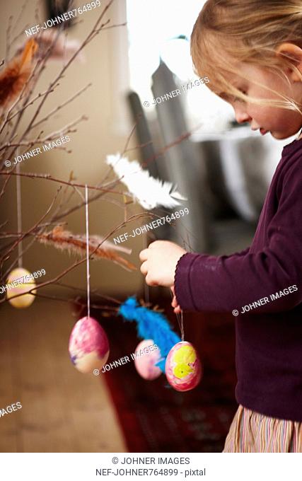 Girl hanging colored eggs in a twig with feathers, Sweden