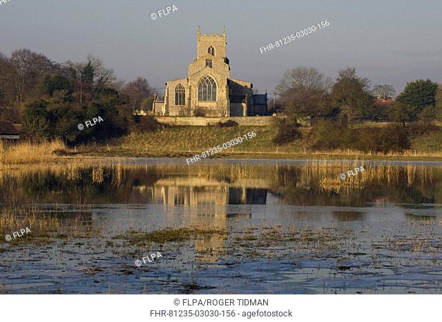 View across flooded grazing marsh towards church, St Mary's Church, Wiveton, Norfolk, England, march