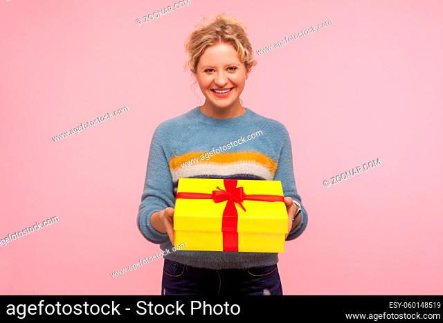 Portrait of happy excited woman with short curly hair in warm sweater holding wrapped present box and smiling at camera, showing winter holiday gift