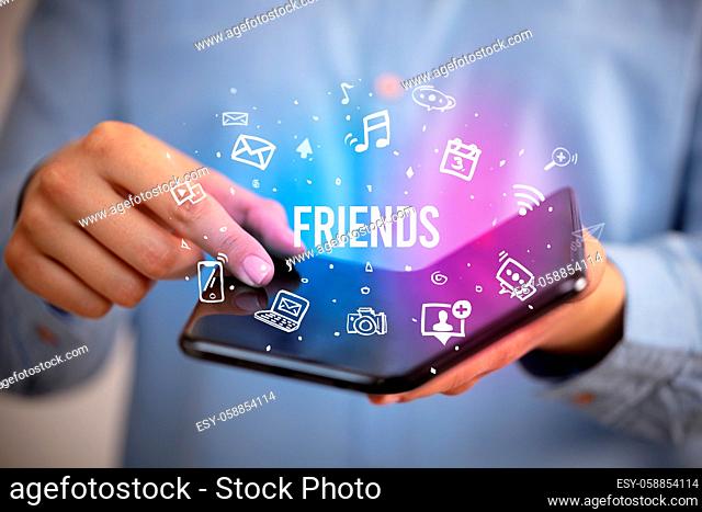 Businessman holding a foldable smartphone with FRIENDS inscription, social media concept