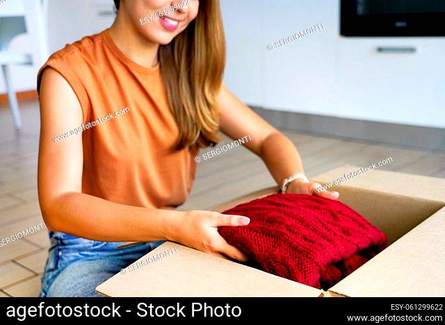 Pretty young woman preparing donation box with clothing. Second hand clothes concept