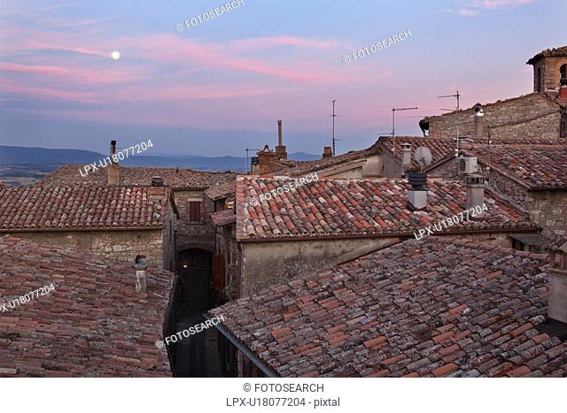 View over traditionally red-tiled terracotta rooftops and narrow street of medieval stone village to hills beyond Tiber valley at sunset
