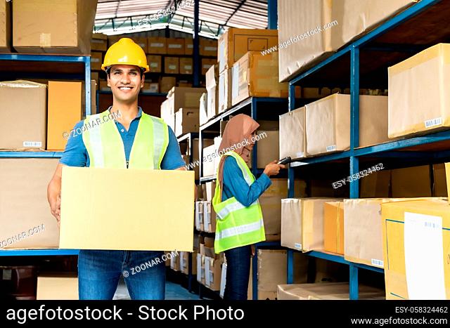 Portrait of Indian warehouse worker hold cardboard box packaging with muslim asian worker do inventory in warehouse distribution center environment