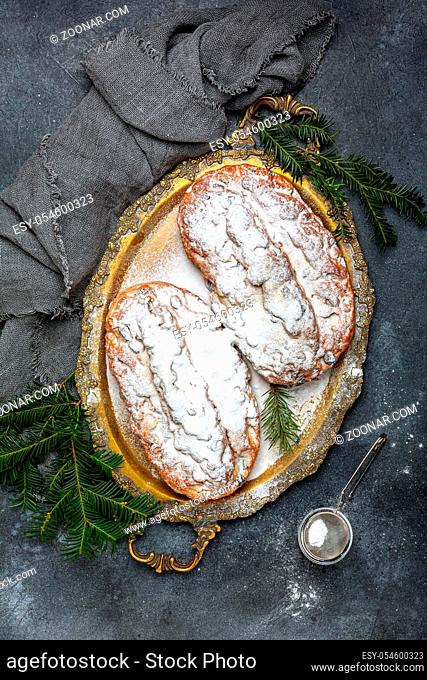 Christmas Stollen sprinkled with powdered sugar, served on a metal tray. Dark textured background, top view. Flat lay