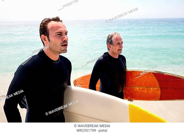 Father and son in wetsuit holding a surfboard looking at sea