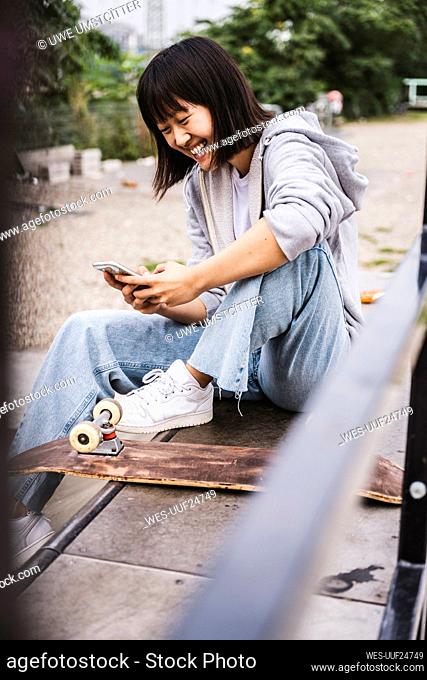 Cheerful teenage girl using smart phone while sitting on bench