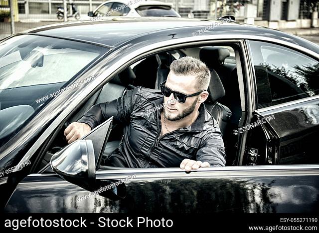 Portrait of young bearded man in sunglasses getting out of his new stylish polished car outdoor