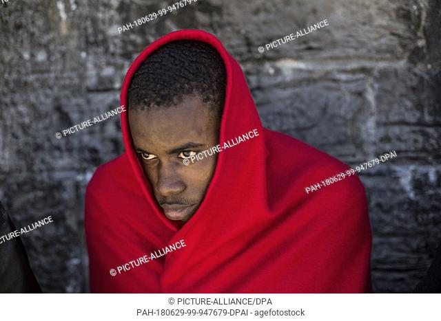 29 June 2018, Spain, Tarifa: An African migrant sits at the port of Tarifa covered in red blankets after being rescued from the Strait of Gibraltar
