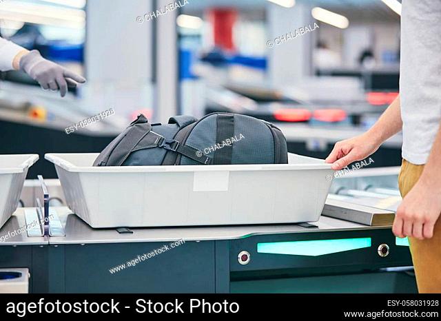 Airport security check. Young man (traveler) waiting for x-ray control his luggage
