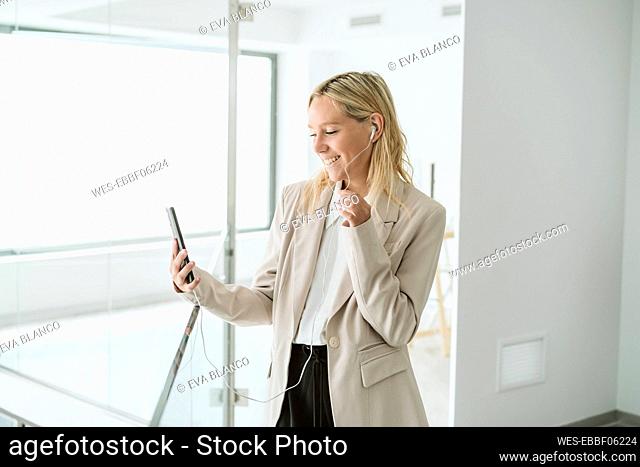 Smiling businesswoman looking at mobile phone in office corridor